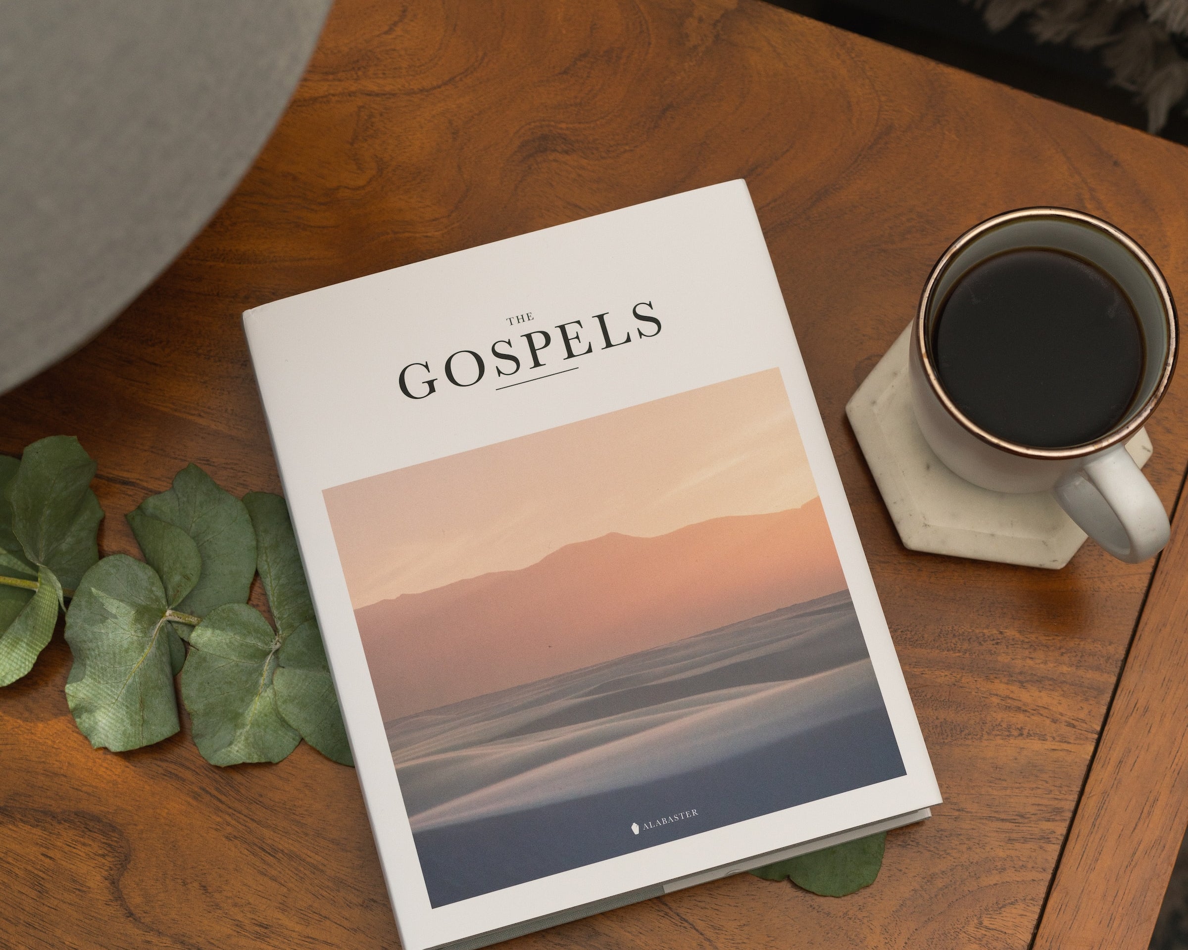 Alabaster's Gospels Hardcover on a coffee table by a cup of coffee