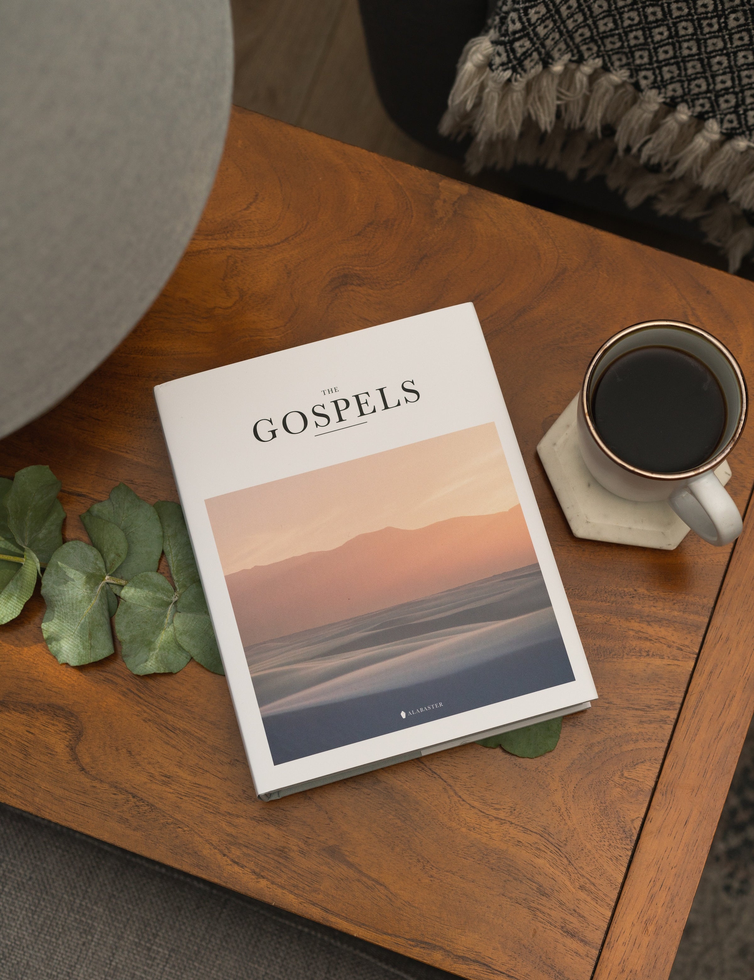 Alabaster's Gospels Hardcover on a coffee table by a cup of coffee